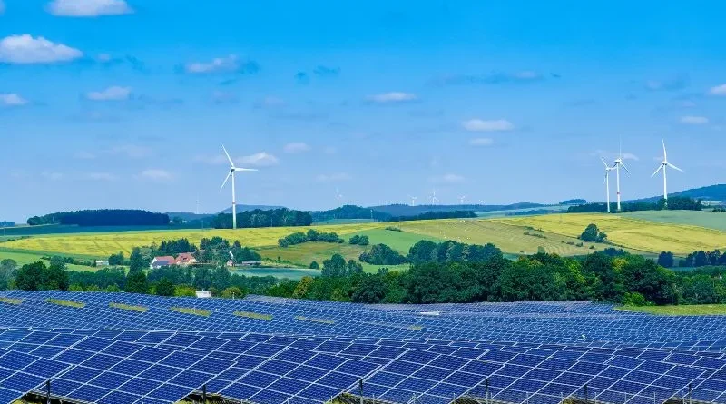 Área campestre com painéis solares e cata ventos sob céu azul