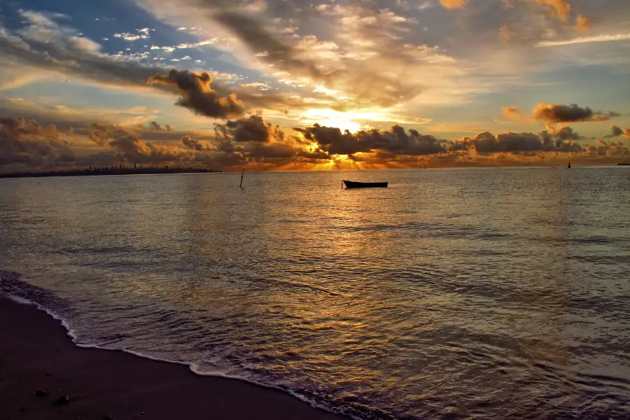 Pôr do sol dourado na Praia de Itaparica com barco de pesca silhueta no mar, ideal para ilustrar o turismo.