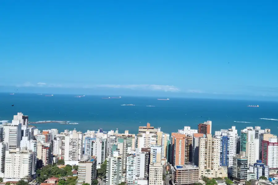 Vista panorâmica da orla e prédios da Praia de Itaparica, Vila Velha, com navios cargueiros no horizonte do Oceano Atlântico.